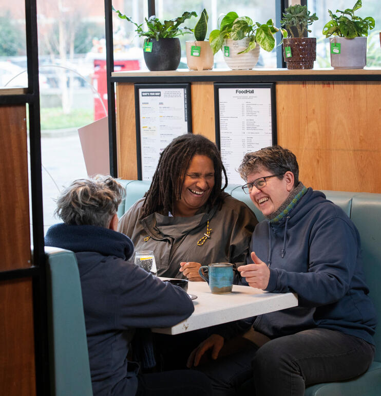 3 people sitting at a table in a cafe drinking coffee. they are smiling and laughing.
